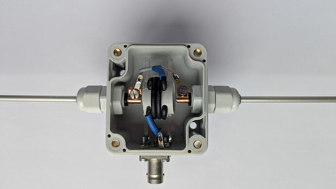 Der Strahler mit dem Balun ist wohl das komplizierteste Element. Für die Durchführung und Halterung der 4mm Aluminium Stäbe habe ich passende Kabeldurchführungen verwendet. Der Balun besteht aus vier Windungen RG-174 (es geht auch irgendein anderes 50Ohm Koaxialkabel) auf einem 20mm Durchmesser Rohr. Das Ganze ist in ein RND 455-00155 Polycarbonat-Gehäuse eingebaut. Dieses Gehäuse ist auch noch ein bisschen wasserdicht (IP65).